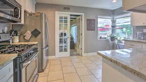 A modern kitchen with stainless steel appliances, a marble countertop, and a view to the backyard.