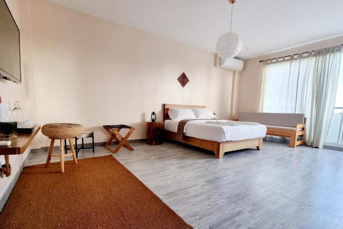 A modern hotel room with a bed, a desk, a chair, a TV, and a large window with curtains.