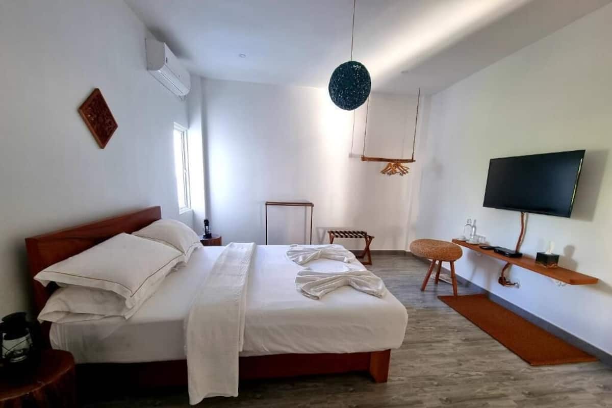 A modern bedroom with a large bed, a TV, and a small seating area.