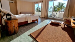 A hotel room with a bed, a wooden side table, a large window with a view of palm trees, and a balcony with outdoor furniture. - Lea Spa Hotel (Maafushi)