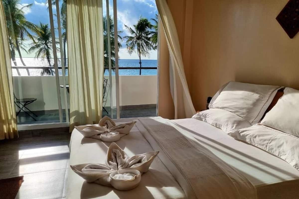 A hotel room with a bed, a view of the beach, and a table with towels.