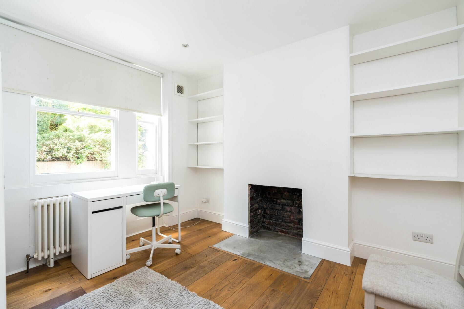 Een moderne kamer met een bureau, stoel, open haard en inbouwplanken.