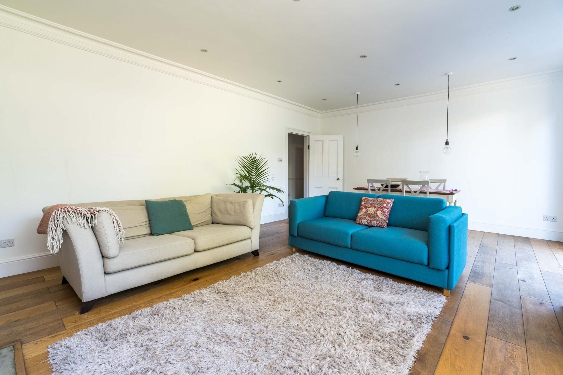Una sala de estar con un sofá beige, un sofá verde azulado, un tapete mullido y piso de madera.