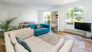 Een ruime woonkamer met een beige bank, een smaragdgroene bank en een witte radiator.