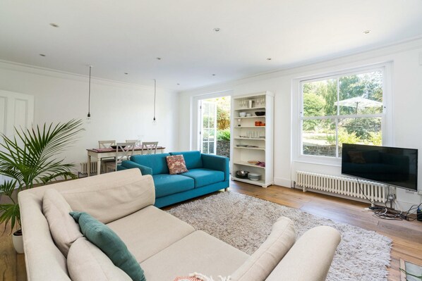 A spacious living room with a beige sofa, a teal sofa, and a white radiator.