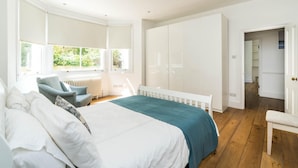 Een slaapkamer met een groot bed, een stoel, een kledingkast en uitzicht op groen.
