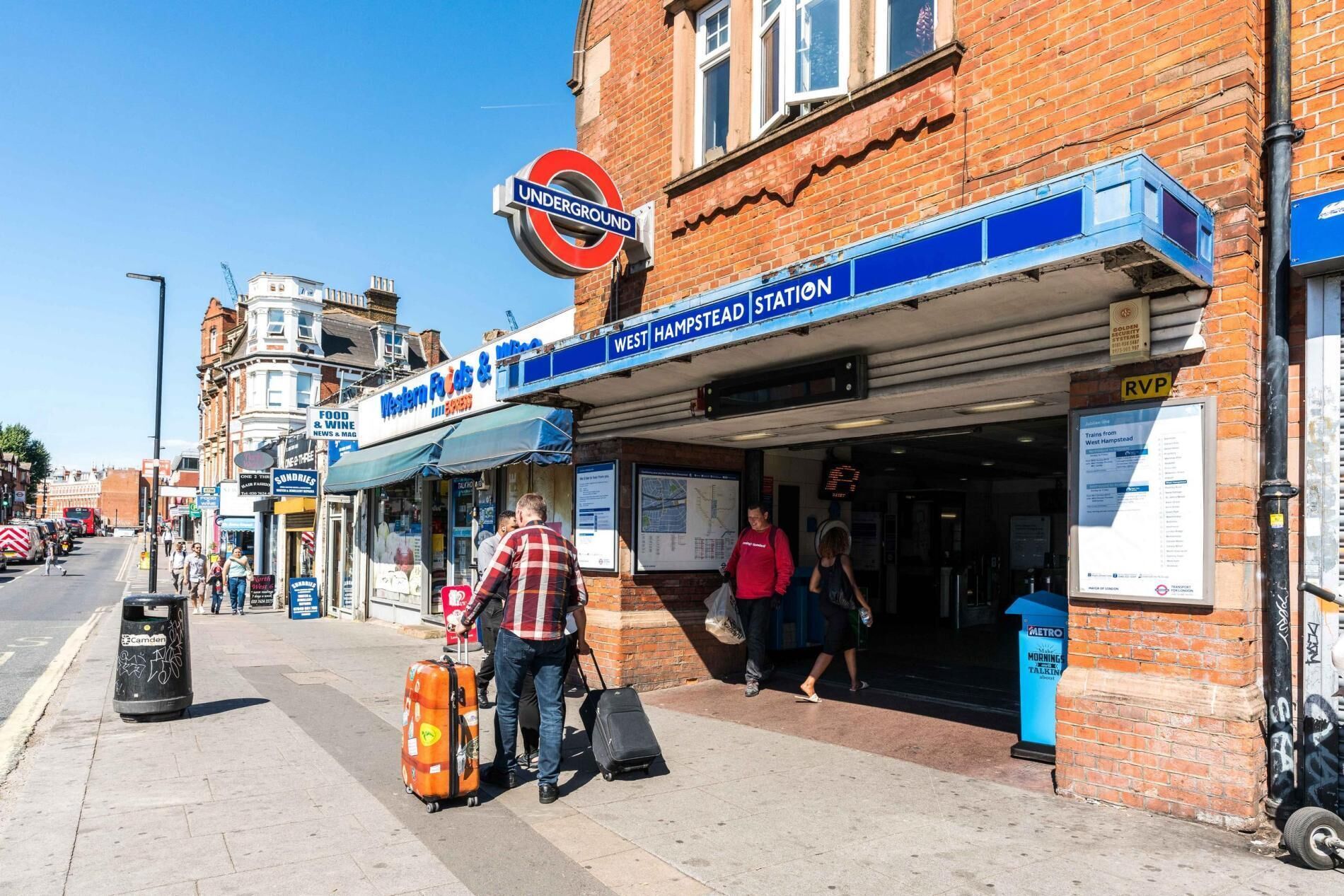 Entrada a una estación de tren con un cartel que indica 'West Hampstead Station' y una tienda cercana llamada 'Western Foods & Wine'.