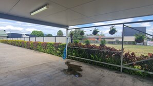Área externa coberta com piso de concreto, plantas em vasos e vista para edifícios e árvores ao fundo.
