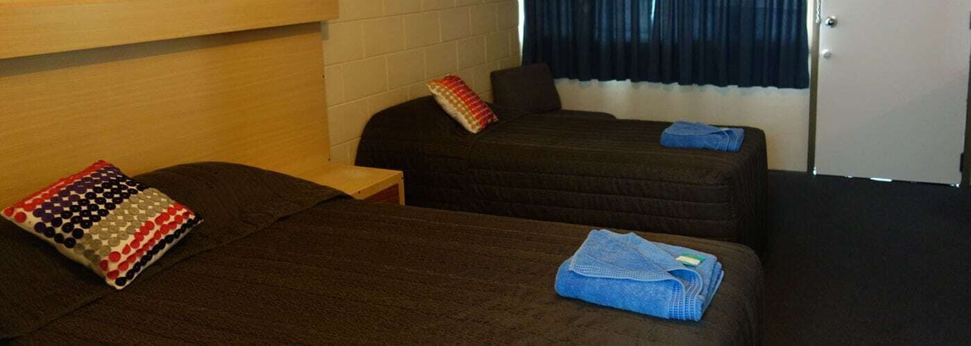 A hotel room with two beds, a wooden headboard, a small table, and a window with curtains.