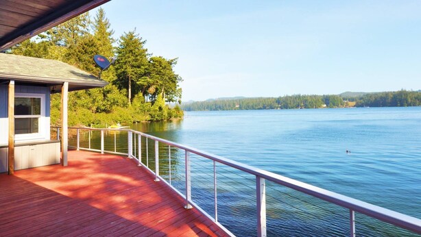 A wooden deck with a railing overlooking a calm lake, surrounded by trees and a clear sky. - New Listing! Adorable lakefront cabin, private dock, hot tub, gas grill, amazing views (Florence)