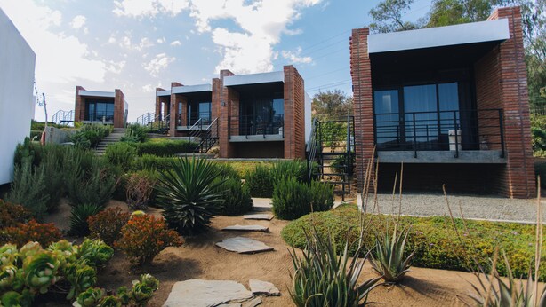 A modern building with brick and glass architecture, featuring a garden with various plants and a stone pathway.