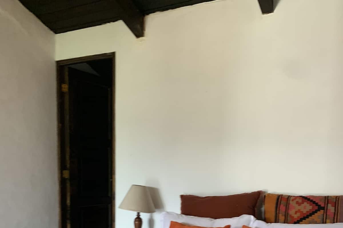 Un dormitorio con cama, almohadas, una mesita de noche, una lámpara y una puerta.