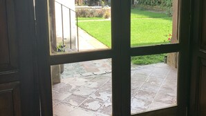 Une vue à travers une fenêtre à cadre en bois, donnant sur un patio en pierre et une cour verdoyante.