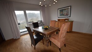 Un coin repas avec une table en bois, deux chaises, un saladier rempli de fruits et une vue sur l’extérieur grâce à une grande fenêtre.