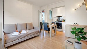 En moderne stue med en sofa, et spisebord og et køkken i baggrunden.