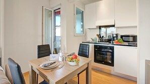 Et moderne køkken med hvide skabe, en mikrobølgeovn og en komfur. Der er et spisebord med stole og en skål med frugt.