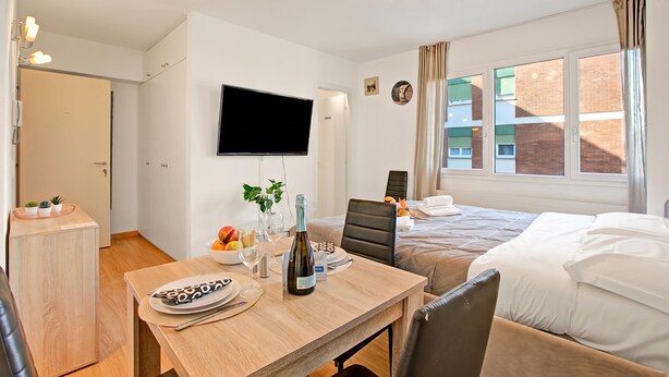 Et hotelværelse med en seng, et skrivebord med en flaske, en stol, et fjernsyn og et vindue.