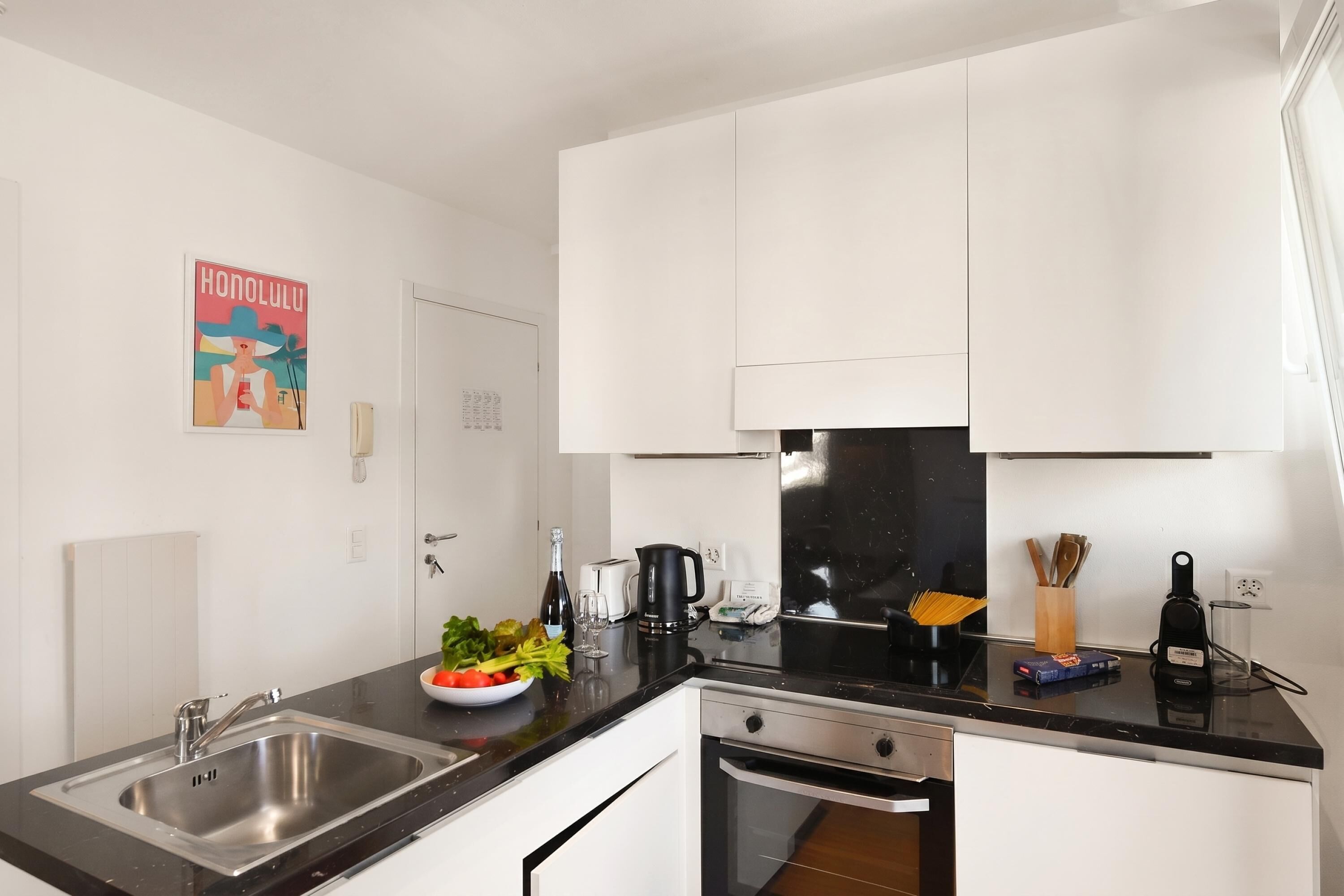 A modern kitchen with a black countertop, stainless steel sink, and white cabinets.