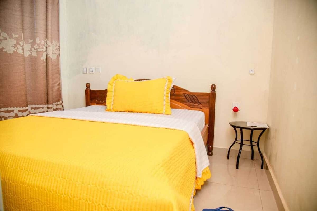 A bedroom with a wooden bed, a yellow bedspread, and a small table with a red object on it.