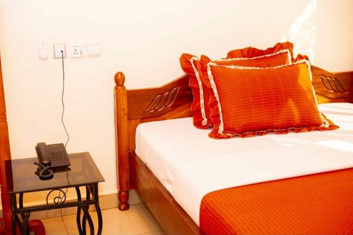 A hotel room with a wooden bed, a bedside table with a telephone, and a power outlet on the wall.
