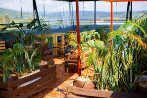 A covered outdoor seating area with wooden benches and potted plants, overlooking a scenic landscape. - NOVALAND HOTEL (Kigali)