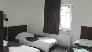 A room with two beds, a window with curtains, a radiator, and a chair. - Hotel Restaurant Villa Romana (Hainburg)
