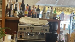 A bar area with a coffee machine, various bottles, and a counter with a napkin dispenser. - Hotel Restaurant Villa Romana (Hainburg)