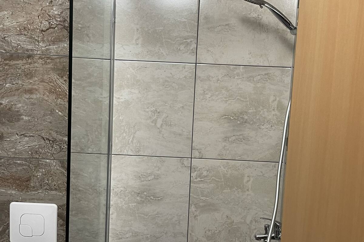 A glass-enclosed shower with a handheld showerhead, a control panel, and a wall-mounted faucet.