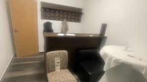 A small, private room with a wooden door, a coat rack, a patterned chair, a black sofa, and a table with a white tablecloth. - Hotel Restaurant Villa Romana (Hainburg)