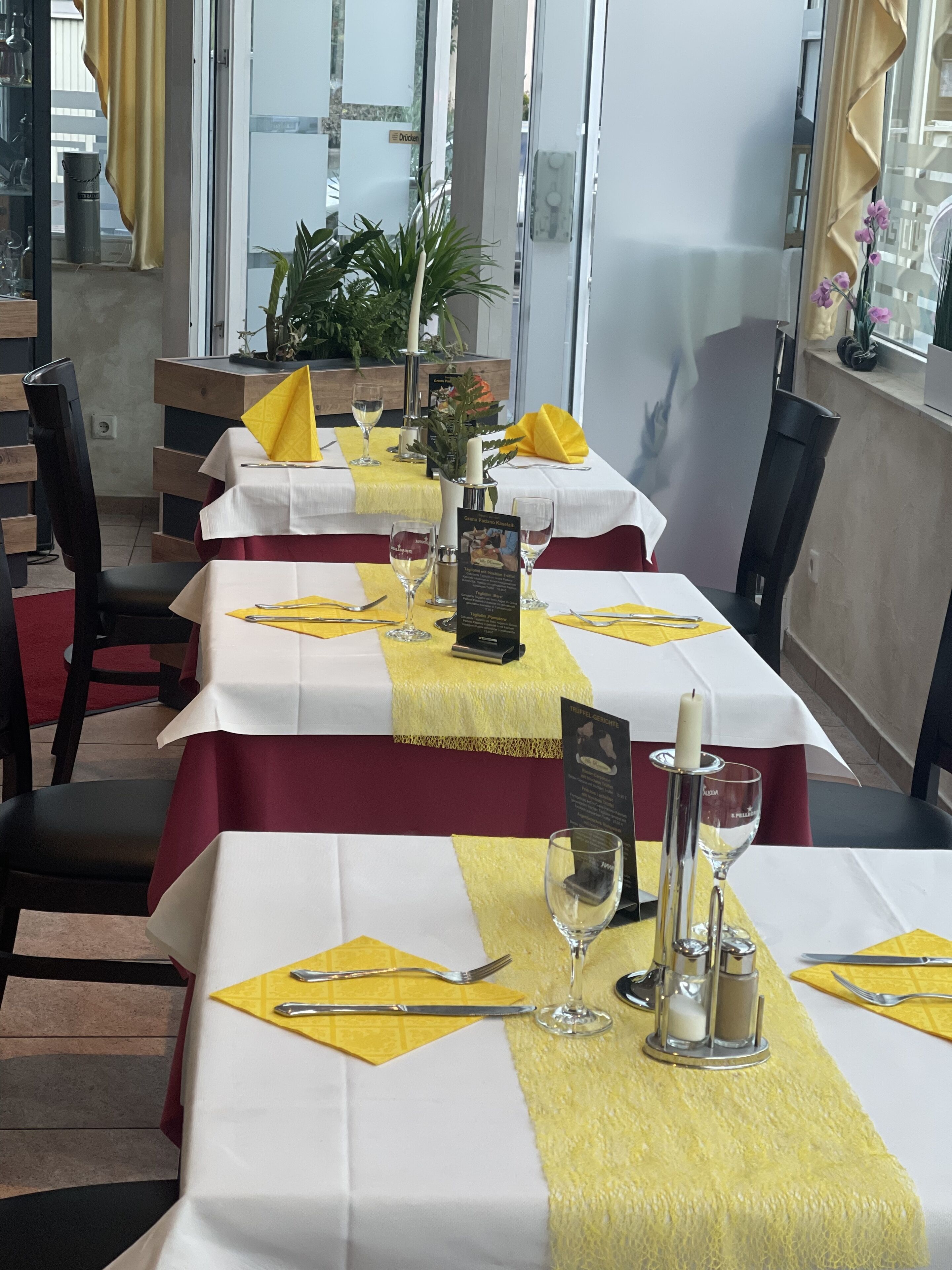 A restaurant with tables set for dining, featuring yellow napkins and white tablecloths.