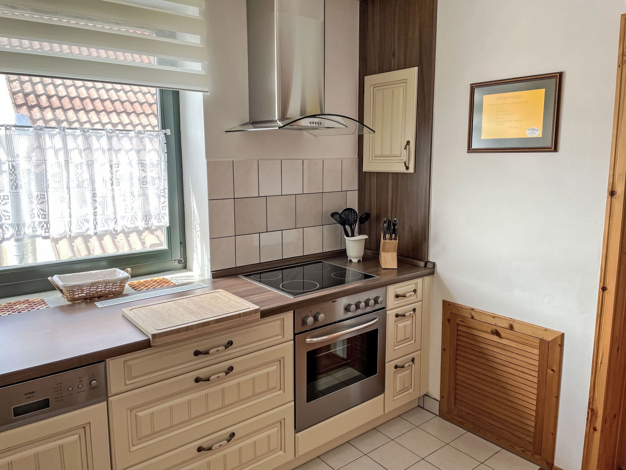 A kitchen with a built-in oven, a stovetop, and a window with curtains.