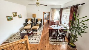 Een gezellige woonkamer met een zithoek, een eettafel met stoelen, een plafondventilator en een potplant.