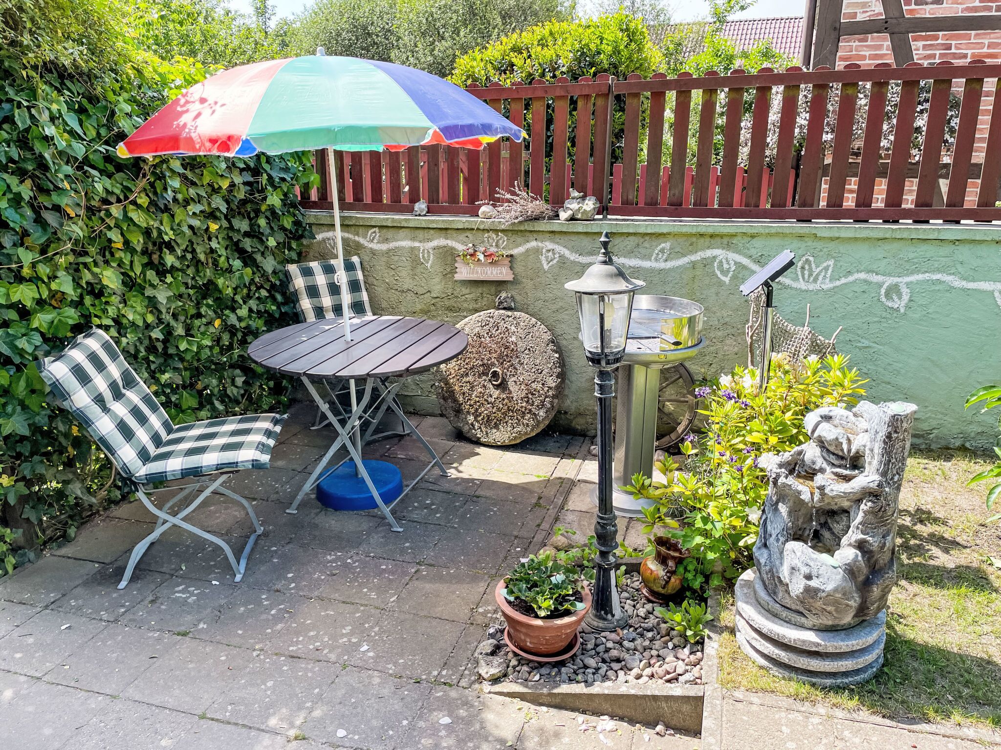 Een terras met een tafel en stoelen, een decoratieve lantaarn en een welkomstbord.