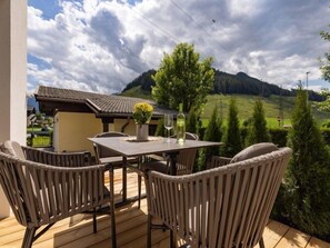 An outdoor patio with a table and chairs, a bottle of wine, and a vase of flowers.