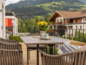Ein Balkon mit einem für zwei Personen gedecktem Tisch, mit Korbstühlen und einer Vase mit gelben Blumen.