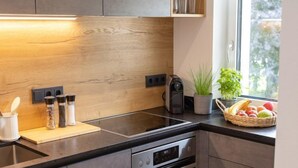 Una cocina moderna con protector de salpicadero de madera, encimeras negras, horno empotrado y ventana con vistas a árboles.