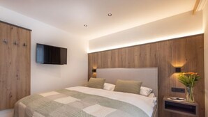Un dormitorio moderno con una cama grande, paneles de madera en las paredes, un televisor de pantalla plana sobre la cama y una mesita de noche con un florero.