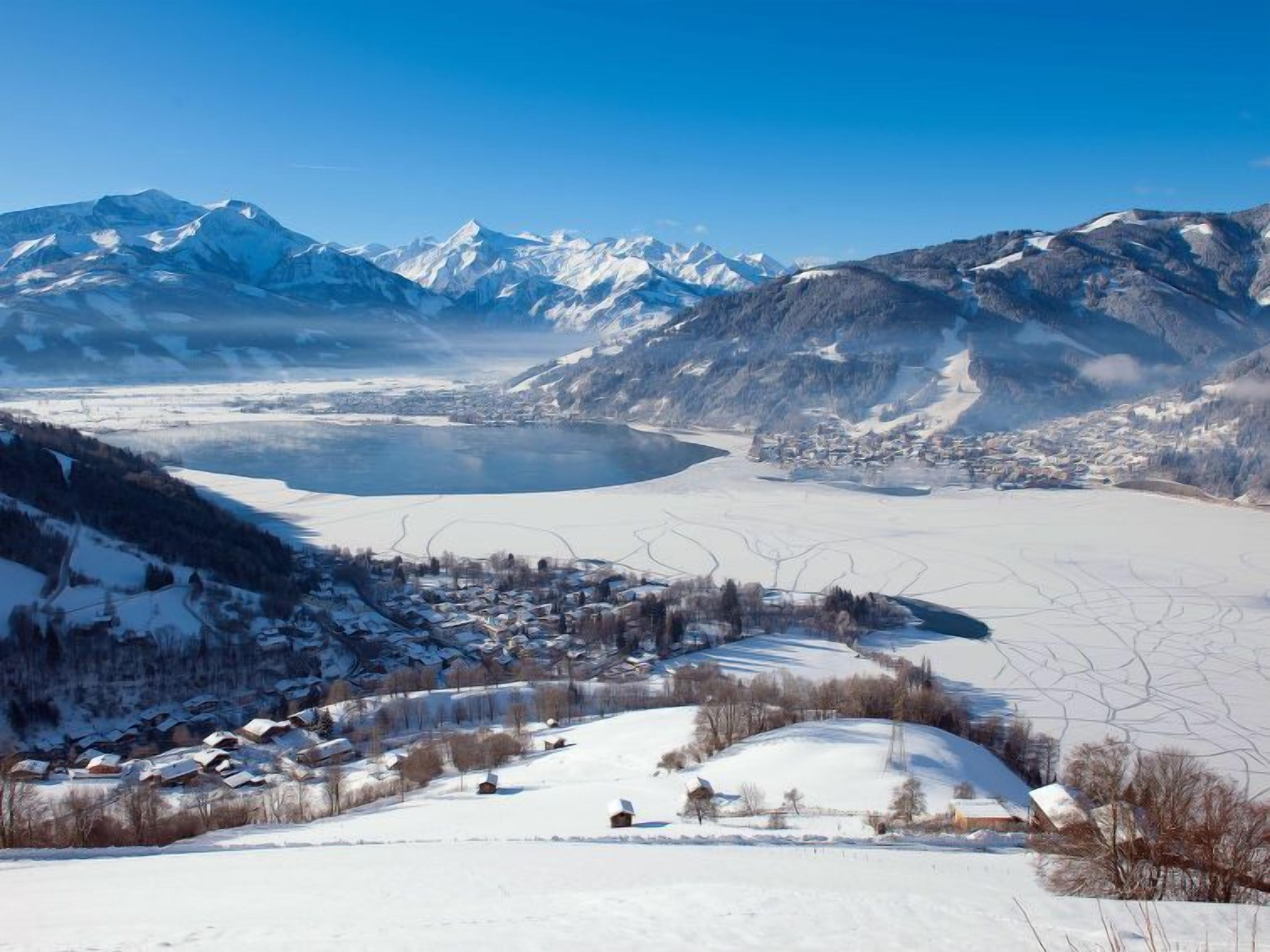 Ein Panoramablick auf eine Berglandschaft mit einem See, schneebedeckten Häusern und einer kleinen Stadt.
