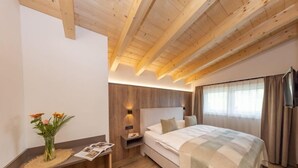 A modern bedroom with a wooden ceiling, a large bed, a desk with a chair, and a nightstand.