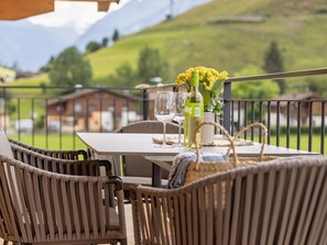 A dining table with chairs, a bottle of wine, and a vase of yellow flowers on a balcony with a mountain view. - Apartment Top 6 by Interhome (Bruck)