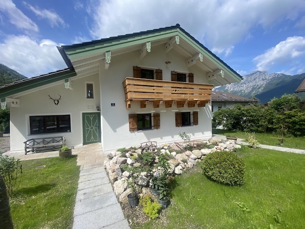 A mountain lodge with a balcony, stone pathway, and a mountain view.