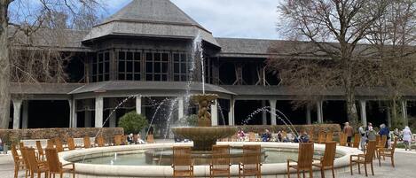Un edificio histórico con una gran fuente en el patio, rodeado de sillas y bancos de madera.