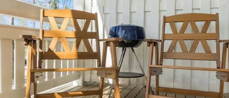 Two wooden chairs with a grill on a wooden deck.