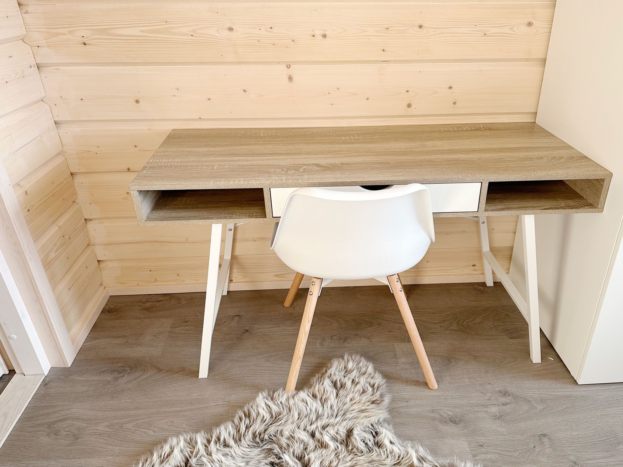 A wooden desk with a white chair, a fur rug on the floor, and a wooden wall.