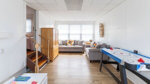Amplia sala de estar con una escalera de madera, dos sofás, una mesa de centro y una mesa para jugar al shuffleboard.