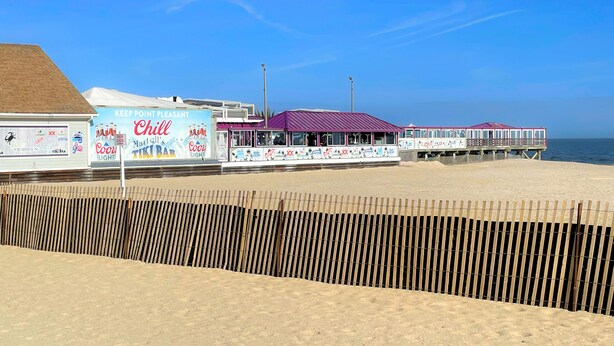 Un paseo marítimo frente a la playa con un bar llamado 'Chill' y un muelle con techo morado.
