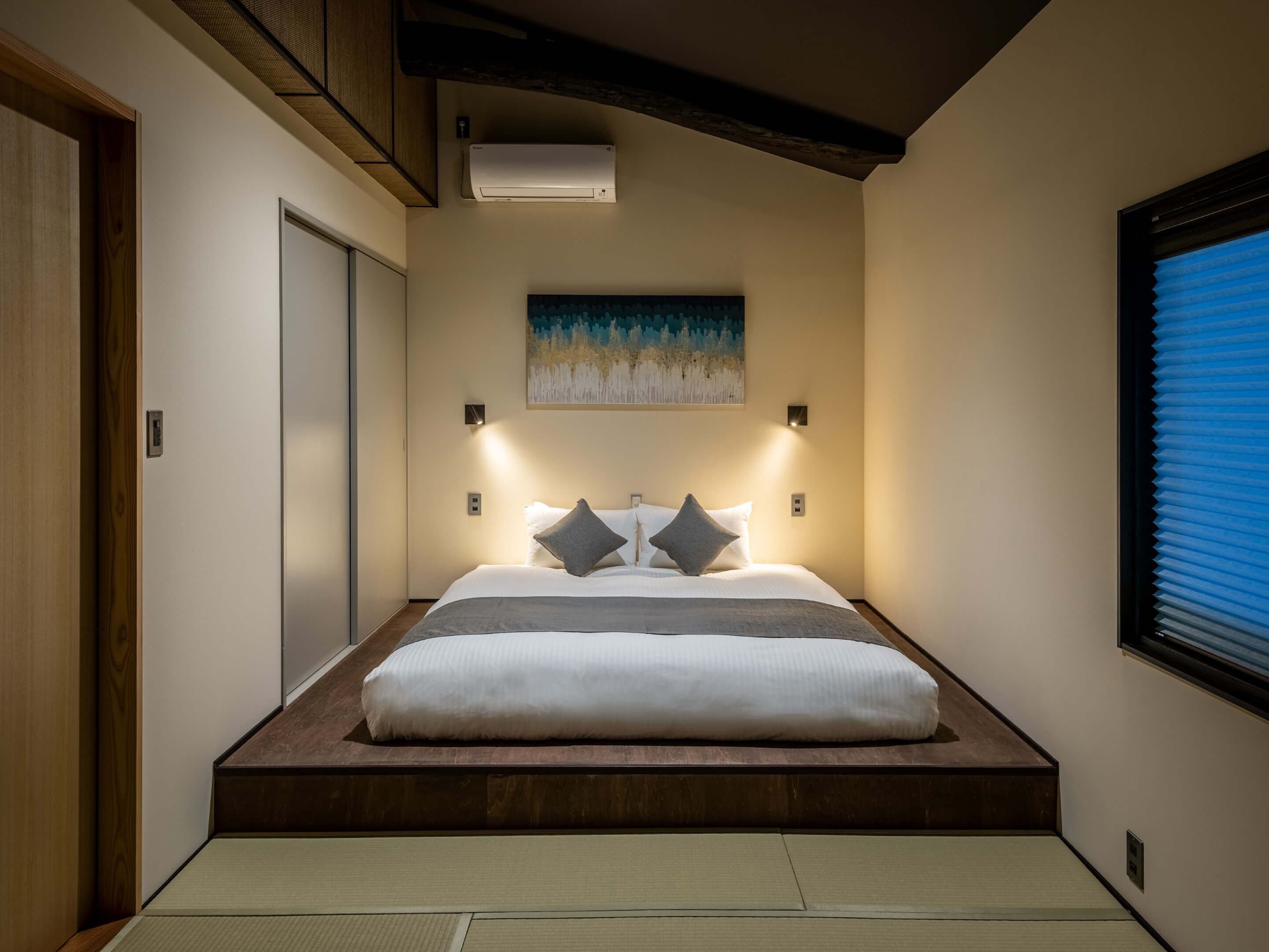 A bedroom with a bed, a painting, and a window with blinds.