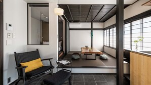 A modern interior with a sofa, a small table with a plant, and a view through a sliding door to another room. - Sansuikyo Machiya House (Kanazawa)