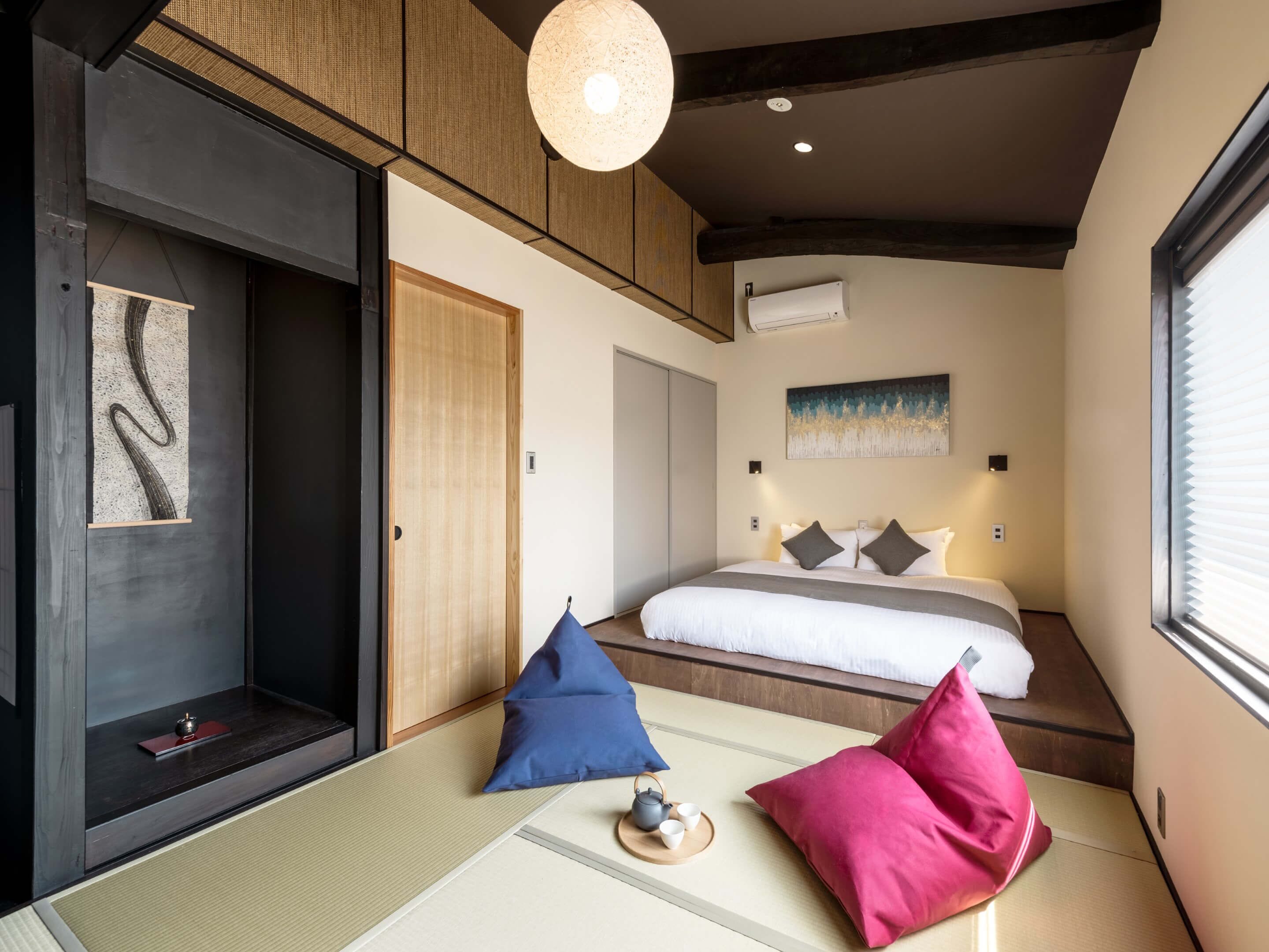 A modern bedroom with a bed, pillows, a tatami mat, a hanging light fixture, and a painting on the wall.