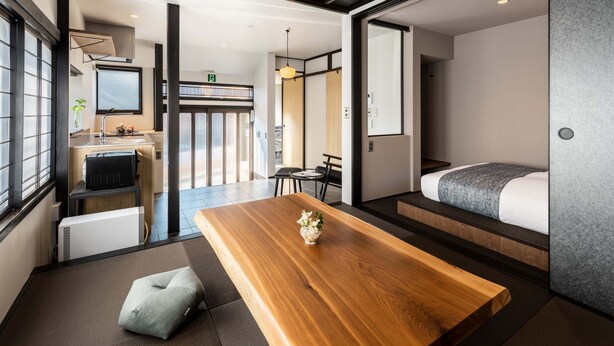 A modern hotel room with a wooden dining table, a sofa, and a bed. - Sansuikyo Machiya House (Kanazawa)